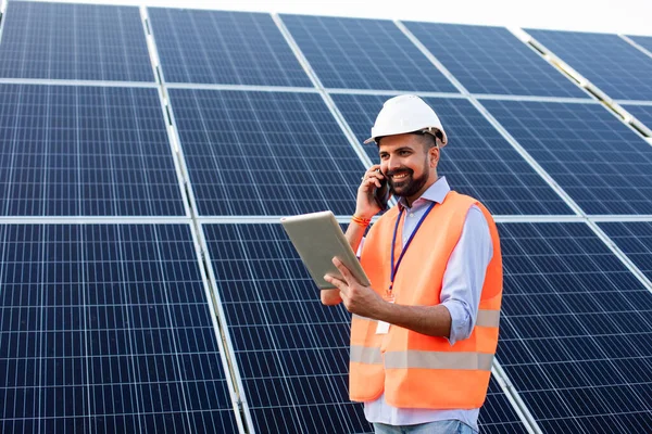Młody elektryk pracuje na stacji słonecznej używając gadżetów. — Zdjęcie stockowe