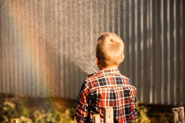 Der Junge genießt einen Regenbogen beim Gießen im Garten — Stockfoto