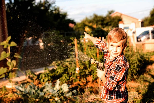 Il ragazzo gode di un arcobaleno mentre innaffia in giardino — Foto Stock