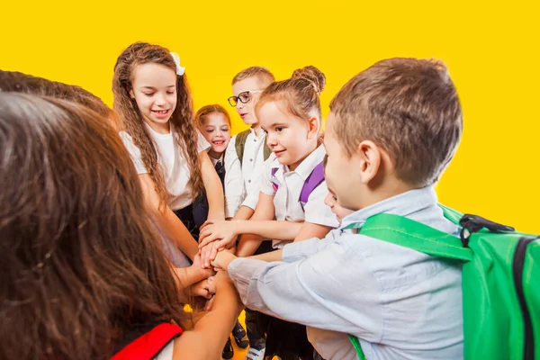 Los niños de la escuela están apilando las manos juntos en el fondo amarillo — Foto de Stock