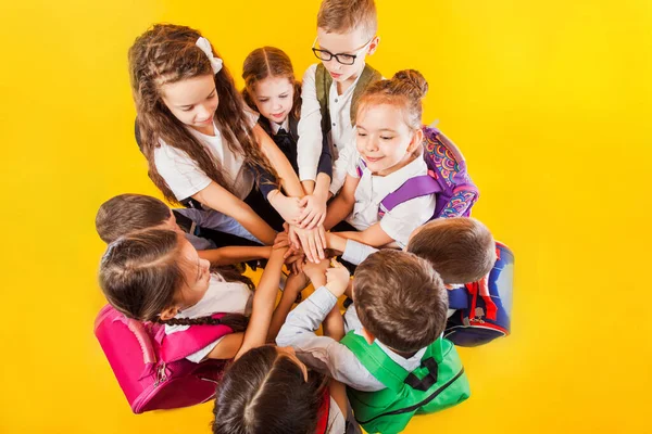 De schoolkinderen stapelen handen samen op de gele achtergrond — Stockfoto