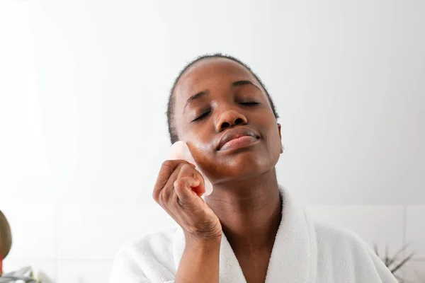 Piękny afrykański dziewczyna masaż twarz z róża kwarc gua sha — Zdjęcie stockowe