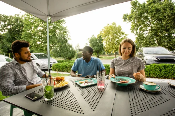 Grupo de amigos multirraciales comiendo en la terraza de la cafetería — Foto de Stock
