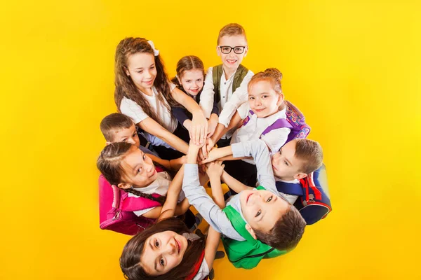 Skolbarnen staplar händerna tillsammans vid den gula bakgrunden — Stockfoto