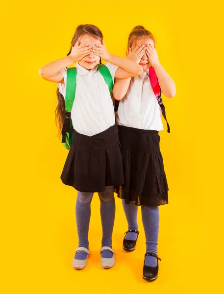 Zwei freundliche Schulmädchen in Uniform halten die Hände auf den Augen — Stockfoto