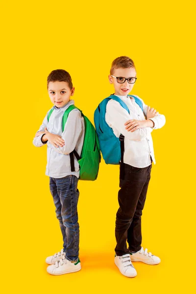 Leuke schooljongens in uniform met rugzakken op gele achtergrond — Stockfoto