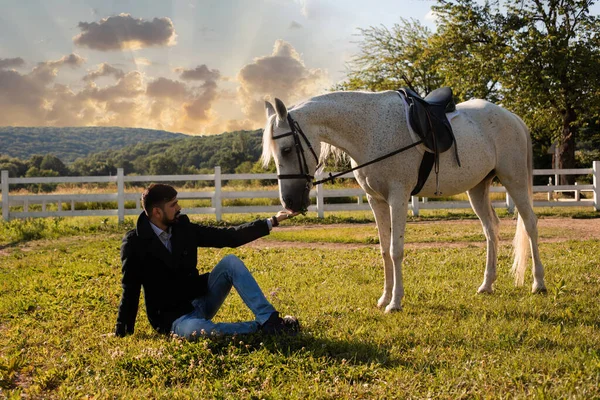 Mann sitzt auf dem Gras und füttert ein Pferd — Stockfoto