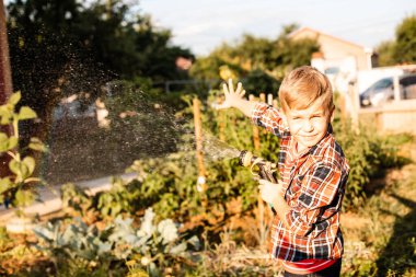 Çocuk bahçede su içerken gökkuşağının tadını çıkarıyor.