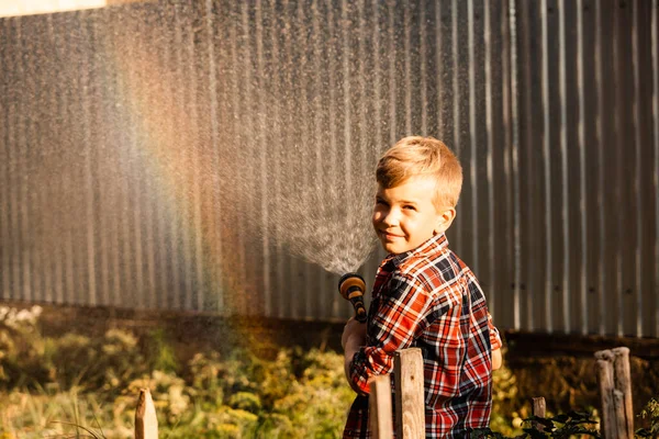 Der Junge genießt einen Regenbogen beim Gießen im Garten — Stockfoto
