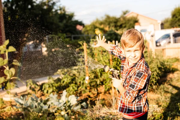 O menino gosta de um arco-íris enquanto rega no jardim — Fotografia de Stock