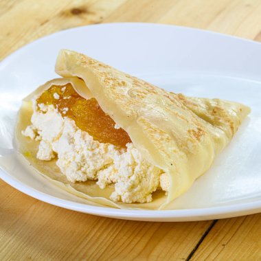 Beyaz tabakta reçel peyniriyle doldurulmuş lezzetli krep manzarasını kapat.