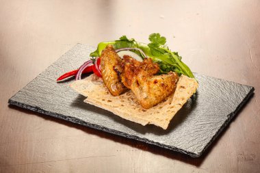 Izgara tavuk kanadı soğan ve kişniş servis edilir.