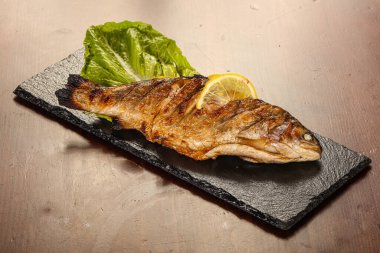 Izgara alabalık, limon dilimi ve salata yaprakları.