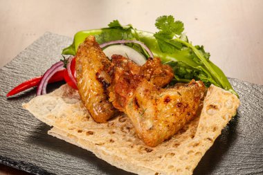 Izgara tavuk kanadı soğan ve kişniş servis edilir.