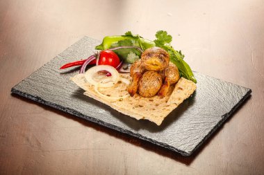 Patates barbeküsü soğan halkaları ve bitkiler servis edilir.