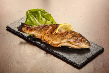 Izgara alabalık, limon dilimi ve salata yaprakları.