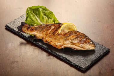 Izgara alabalık, limon dilimi ve salata yaprakları.