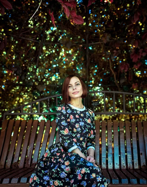 Yeşil yaprakları arka plan karşı bir bankta oturan güzel kadın — Stok fotoğraf