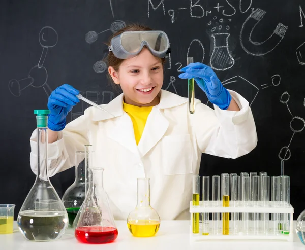 Schoolgirl in white gown doing experiments with liquids — Stock Photo, Image