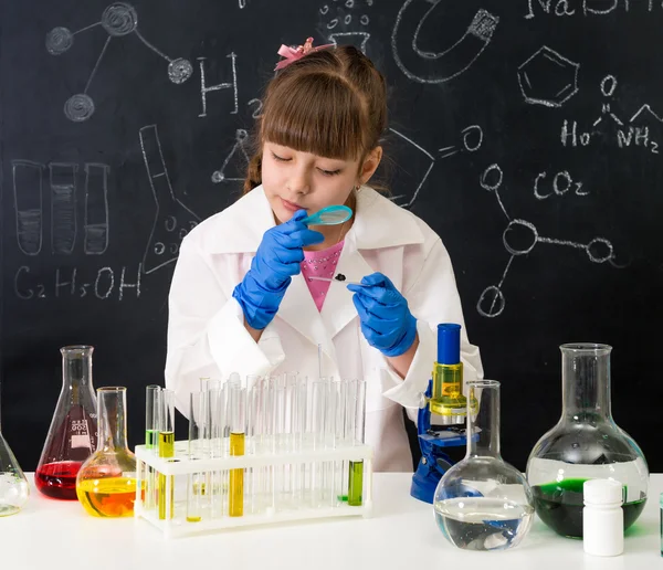 Little schoolgirl looking through magnifier on reagents — Stock Photo, Image