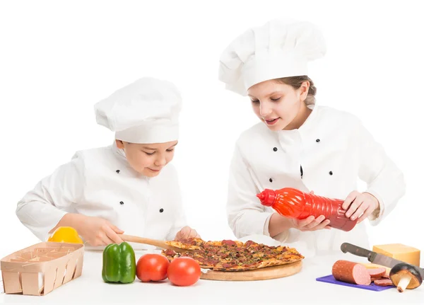 Menino e menina de uniforme branco à mesa com pizza — Fotografia de Stock