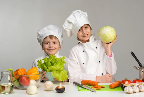 Two smiling children-cooks by the table with vegetables — Stock Image Two smiling children-cooks by the table with vegetables Stock Picture