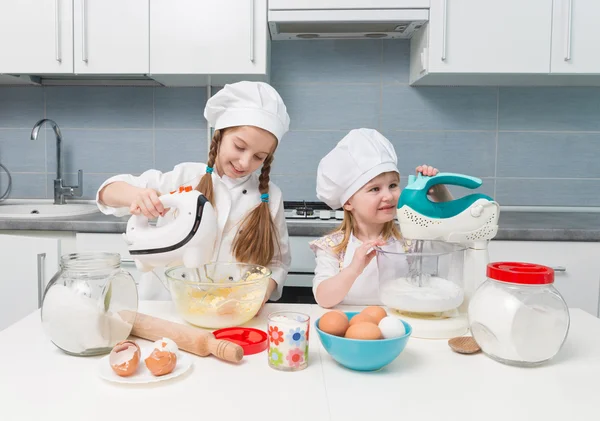 Twee kleine meisjes in chef-kok uniform met ingrediënten op tafel — Stockfoto