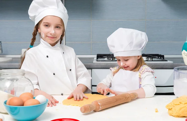 Twee kleine meisjes in chef-kok uniform met ingrediënten op tafel — Stockfoto