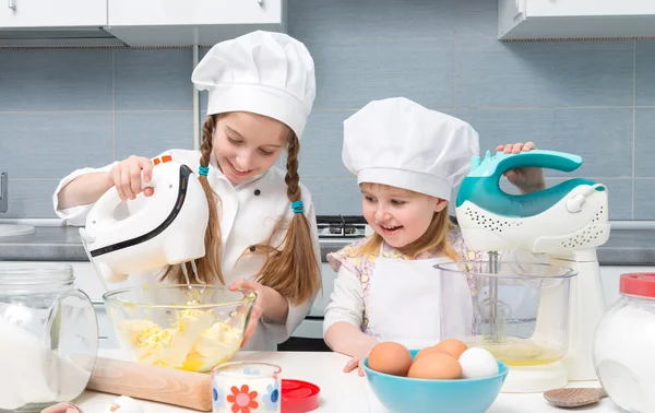 Two little girls in chef uniform with ingredients on table — Stock Photo, Image