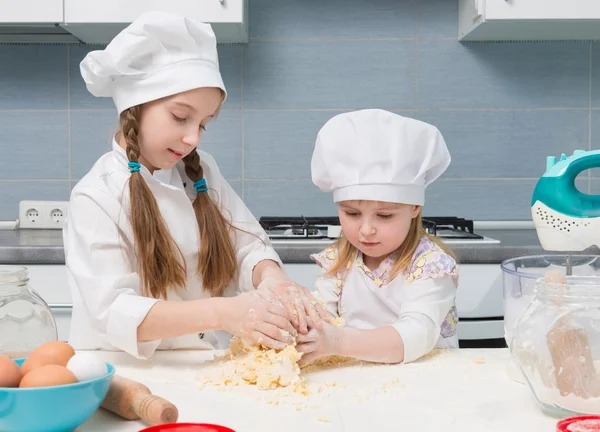 Twee kleine meisjes in chef-kok uniforme kneed het deeg — Stockfoto