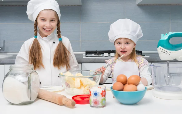 Zwei kleine Mädchen in Kochuniform mit Zutaten auf dem Tisch — Stockfoto