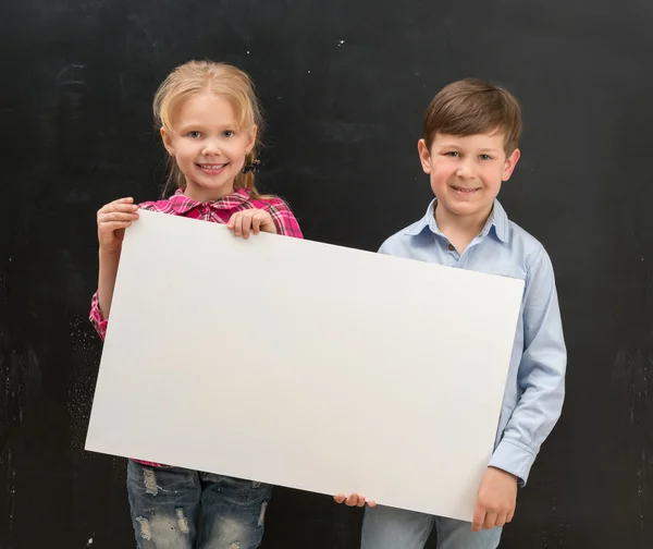 Dos escolares sonrientes con hoja de papel en blanco — Foto de Stock