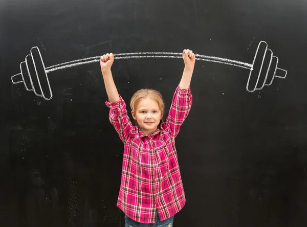 Lovely little girl rising up drawm barbell with two hands — Stock Photo, Image