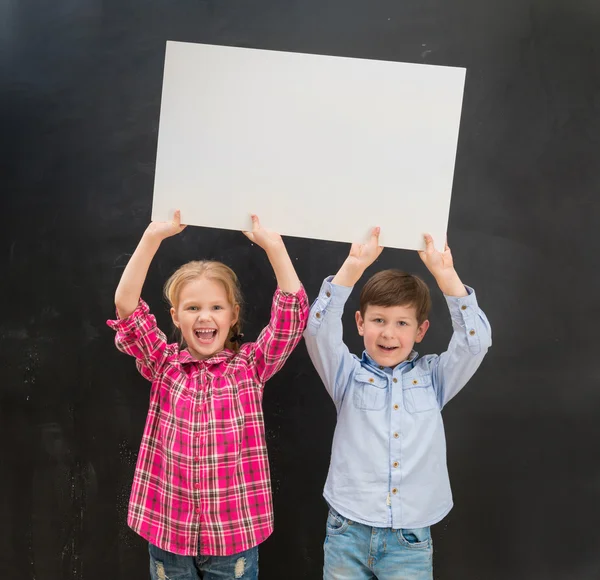 Dos niños pequeños que guardan una hoja de papel en blanco sobre sus cabezas —  Fotos de Stock