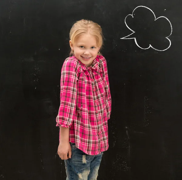 Söt liten skolflicka stående framför tavlan med ritade moln — Stockfoto