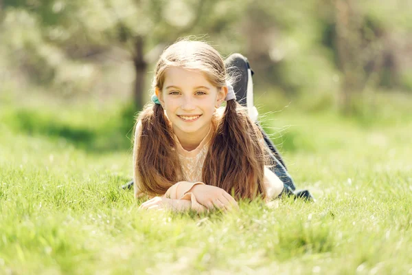 Süßes lächelndes kleines Mädchen, das auf dem Gras liegt — Stockfoto