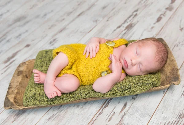 Neugeborenes Baby in gelbem Kostüm schläft auf Holzbett — Stockfoto