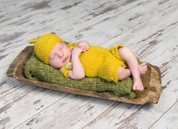 Новорожденный ребенок в жёлтом костюме спит на деревянной кровати — стоковое фото