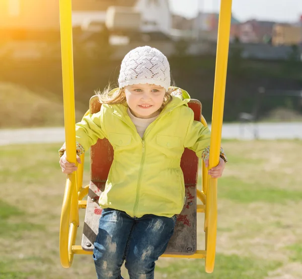 Lovely little girl in yellow coat riding on a swing — Stock Photo, Image