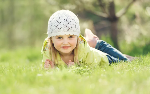 Usměvavá holčička leží na trávníku v parku — Stock fotografie