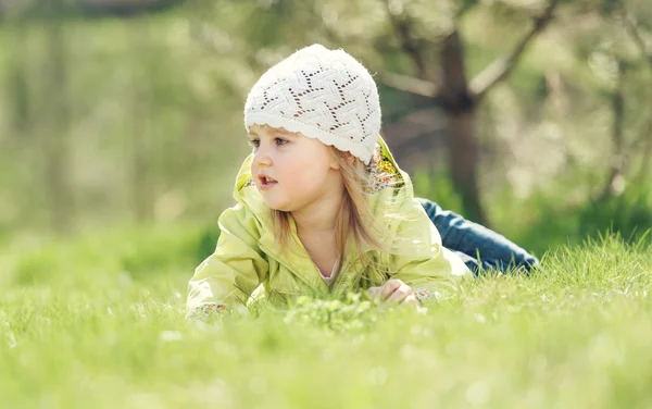 Smiling little girl lying on a lawn in the park — Stock Photo, Image