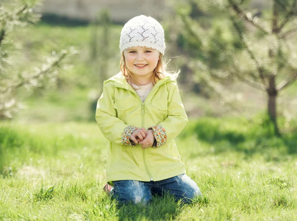 Улыбающаяся маленькая девочка, сидящая на лужайке в парке — стоковое фото