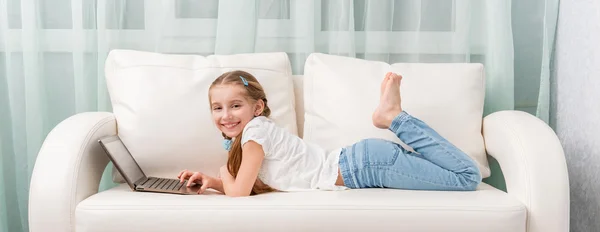 Kleines Mädchen liegt auf Sofa und schaut auf Notizbuch und lacht — Stockfoto