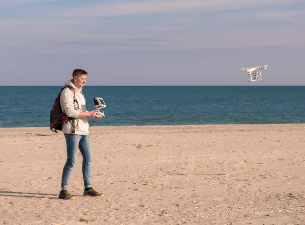 Uomo con zaino gestione quadrocopter in riva al mare — Foto Stock