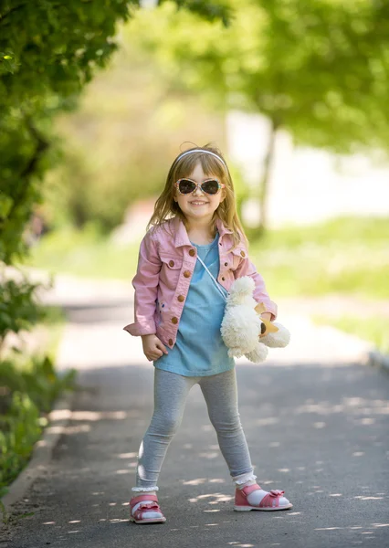 Trendy little girl in park with teddybear in hand — Stockfoto