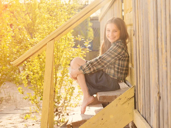 Smiling little girl sitting on wooden stairs barefoot — Stock Photo, Image