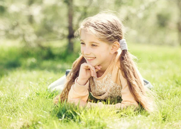 Süßes lächelndes kleines Mädchen, das auf dem Gras liegt — Stockfoto