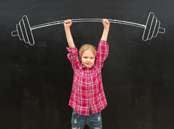 Lovely little girl rising up drawm barbell with two hands — Stock Photo, Image