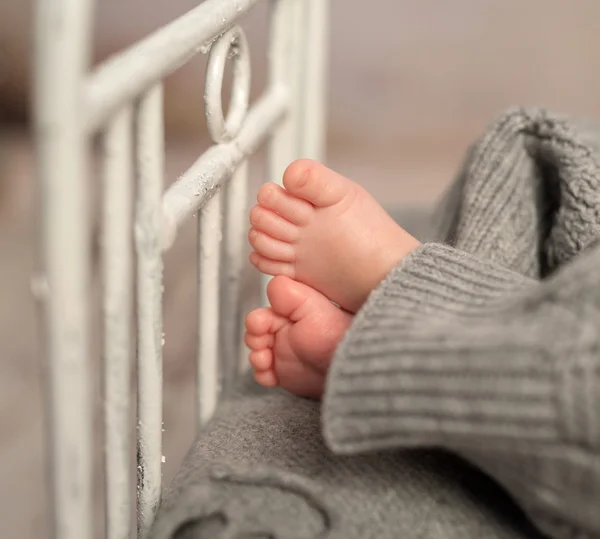 Funny baby fötter av grå byxor på barnsäng — Stockfoto