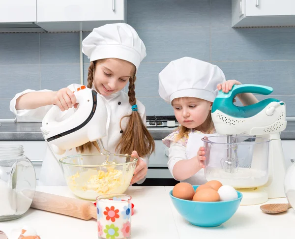 Two little girls in chef uniform with ingredients on table — Stock Photo, Image